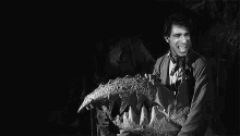 a black and white photo of a man holding a large rock with sharp teeth .