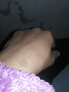 a close up of a person 's hand with a purple sweater behind it