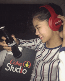 a girl wearing headphones and holding a bottle of coke