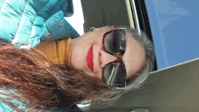 a woman wearing sunglasses and red lipstick is looking out of a car window