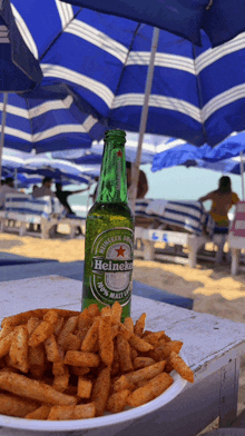 a bottle of heineken sits next to a bowl of fries