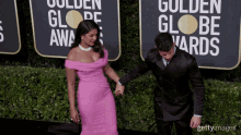 a woman in a pink dress and a man in a black suit are holding hands on the red carpet for the golden globe awards