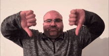 a bald man with glasses is giving a thumbs down sign with both hands .