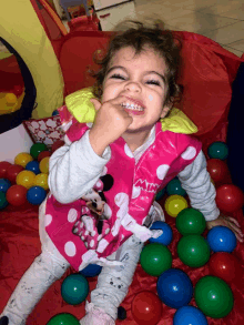 a little girl wearing a pink minnie mouse vest is playing with balls