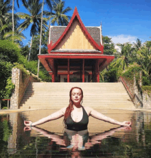 a woman sits in a pool with her arms outstretched in front of a temple