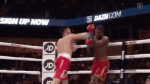 two men are boxing in a ring with a sign that says sign up now in the background .