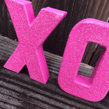 two pink letters x and o sitting on a wooden surface