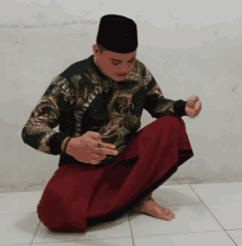 a man wearing a black hat is squatting down with his hands folded