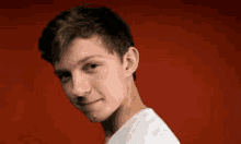 a young man in a white shirt is standing in front of a red background and looking at the camera .