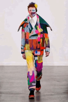 a man wearing a colorful jacket and pants is walking down a runway at a fashion show .