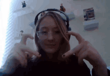 a girl wearing headphones and glasses is making a heart shape with her hands