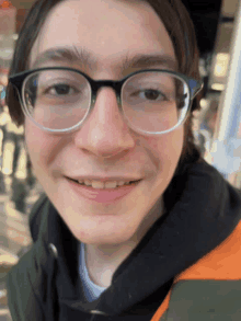 a young man wearing glasses and a black jacket smiles