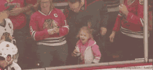 a little girl in a pink jacket stands in front of a hockey player wearing a jersey with the letter c on it