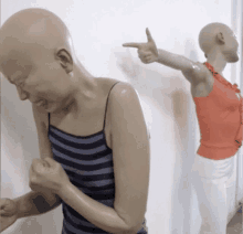 a bald woman in a striped tank top is pointing at another bald woman in an orange shirt