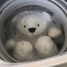 a white teddy bear is in a washing machine filled with soapy water