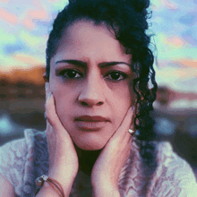 a woman with curly hair is holding her face with both hands