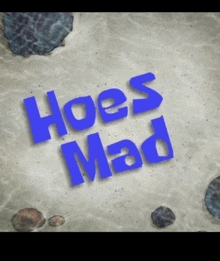 the word hoes mad is written in blue on a sandy surface