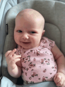 a baby wearing a pink floral bodysuit is smiling