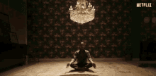 a man is sitting in a lotus position in front of a chandelier in a room .