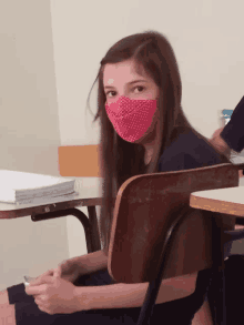 a girl wearing a pink polka dot face mask sits at a desk