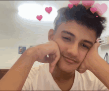 a young man with pink hearts on his head looks at the camera