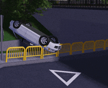 a white car is upside down on the side of the road next to a yellow fence