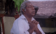 an older man is sitting in a chair with his hands folded in prayer