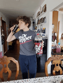 a boy wearing a dr pepper shirt drinks from a glass while holding a bottle of dr pepper