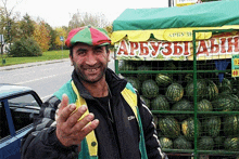 a man wearing a red green and yellow hat is smiling in front of a sign that says apby3