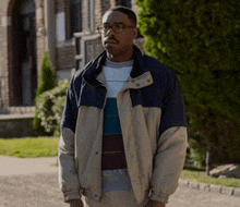 a man wearing glasses and a jacket is standing in front of a building .