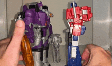 a person is playing with two transformers toys , one of which is purple and one of which is red .