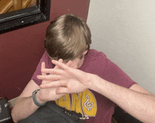 a man wearing a purple shirt with the word ave on it covering his face with his hands