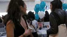 two women talking in front of a table with balloons and a sign that says ' a & b ' on it