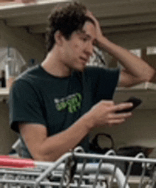 a man in a black shirt is sitting in a shopping cart looking at his phone .