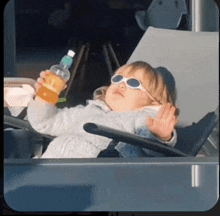 a little girl wearing sunglasses is laying in a chair holding a bottle of orange juice