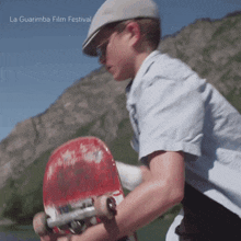 a boy wearing a hat and sunglasses is holding a skateboard in front of a mountain and the words la guarimba film festival