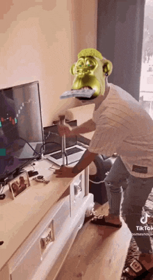 a man wearing a shrek mask is holding a hammer in front of a tv .