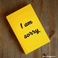 a yellow book that says `` i am sorry '' on a wooden table .