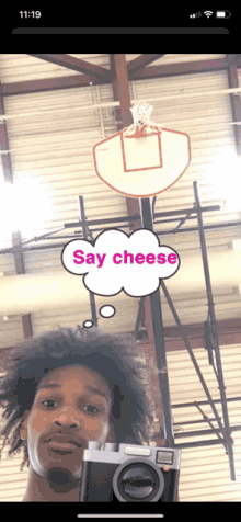 a man taking a picture of a basketball hoop with a speech bubble that says say cheese