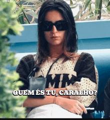 a woman wearing sunglasses and a sweater with the words quem es tu caralho on the bottom