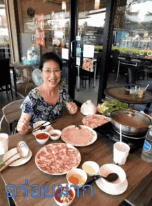 a woman is sitting at a table with plates of food and a sign that says ' อร่อย มาก ' on it