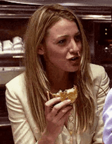 a woman in a white jacket is eating a sandwich in a restaurant .