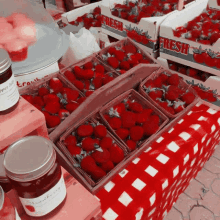 boxes of fresh strawberries sit on a table with jars of strawberry jam