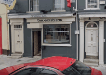 a red car is parked in front of a building called devenish bar