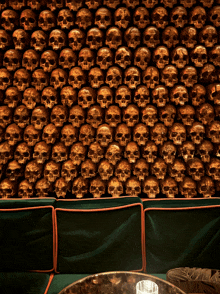 a wall of gold skulls with a green couch in front of it