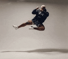 a man is jumping in the air while wearing a black hoodie and shorts .