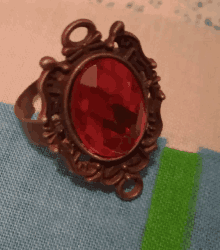 a ring with a red stone in the center is on a table