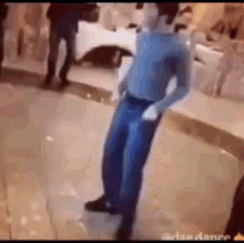 a man in a blue shirt and blue jeans is dancing on a dance floor .