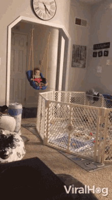 a baby in a swing in a living room with a sign that says family on the wall behind him