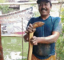 a man in a blue shirt is holding a wooden stick in front of a sign that says " ikan "